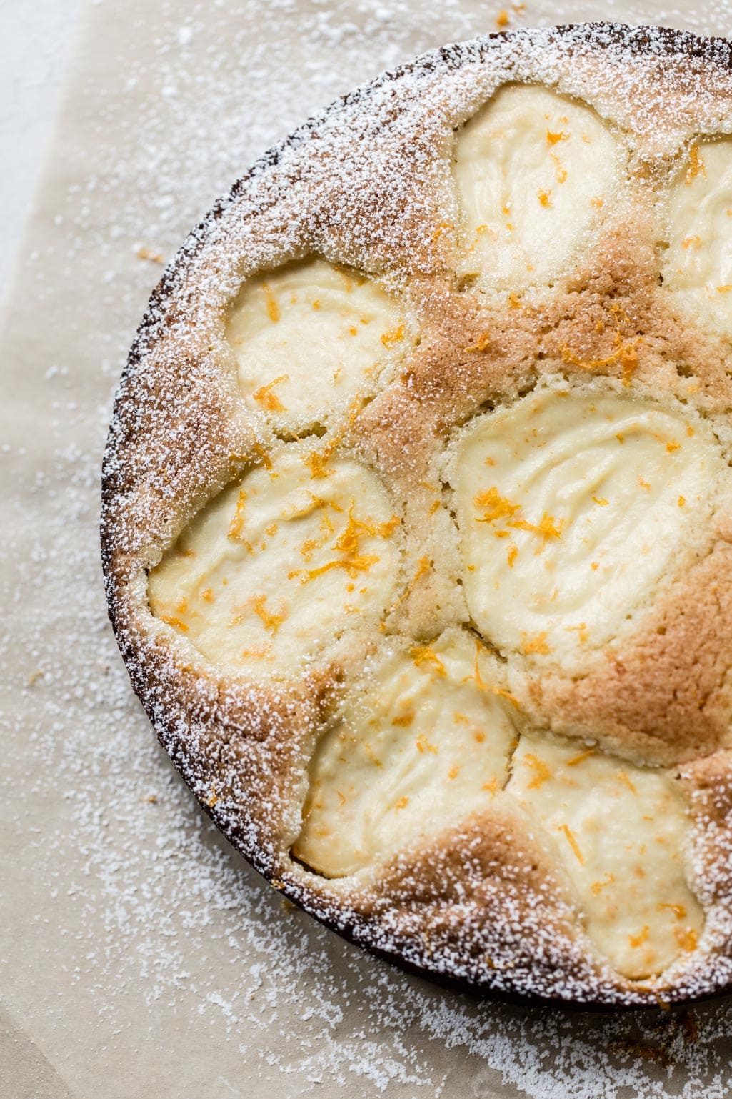 A picture of a cake with ricotta baked into the top, with orange zest and powdered sugar on top.