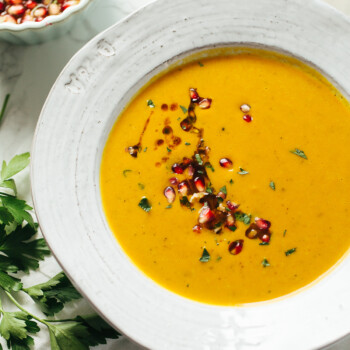 Smooth sweet potato soup in a bowl with pomegranate seeds and fresh cilantro scattered on top.