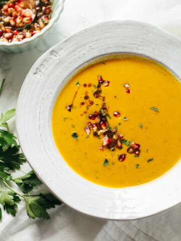 Smooth sweet potato soup in a bowl with pomegranate seeds and fresh cilantro scattered on top.