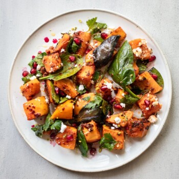 Butternut squash salad on a plate with feta cheese, baby spinach sprinkled with pomegranate seeds and pistachios.