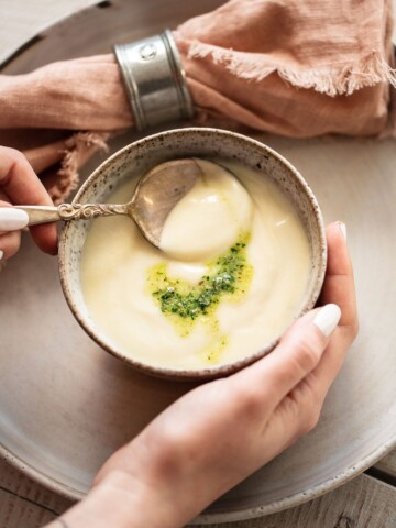 A person's hands cupping a bowl of creamy cauliflower soup.