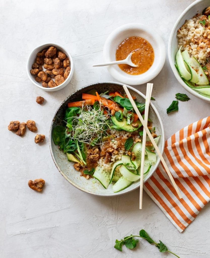 Gray bowl with chopsticks, full of rice salad with avocado, cucumber, carrots and walnut sauce.