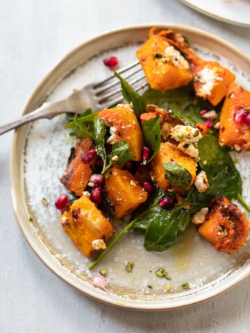 Butternut squash salad on a plate with feta cheese, baby spinach sprinkled with pomegranate seeds and pistachios.
