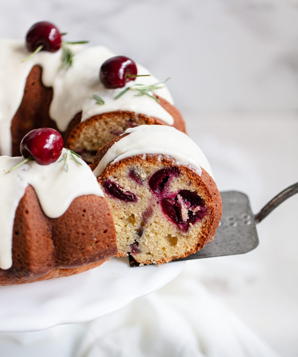 A photo showing an Olive Oil Cake with white icing and fresh cherries on top.