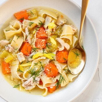 A bowl of chicken noodle soup with chunks of carrots, celery and chopped dill on top.
