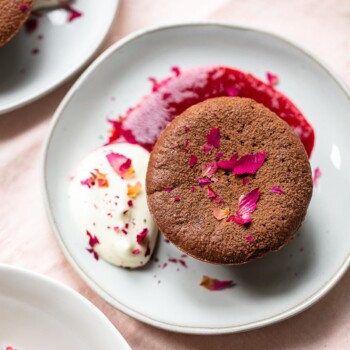 Individual flourless chocolate cake on a small plate, with red raspberry sauce, whipped marscarpone cream and rose petals.