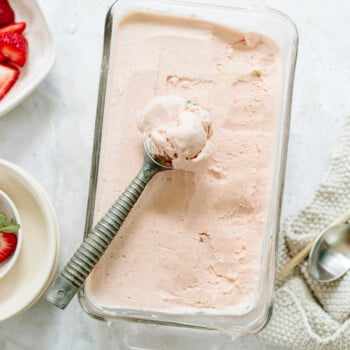 Creamy strawberry ice cream in a glass baking pan with an old-fashioned metal scoop