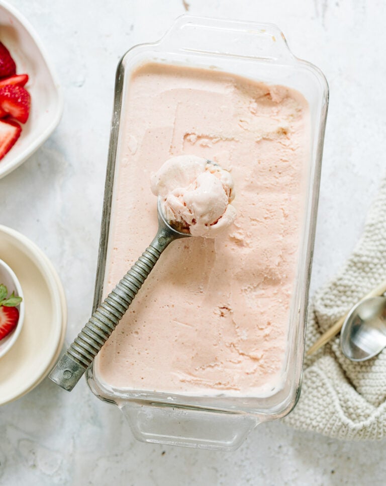 Creamy strawberry ice cream in a glass baking pan with an old-fashioned metal scoop