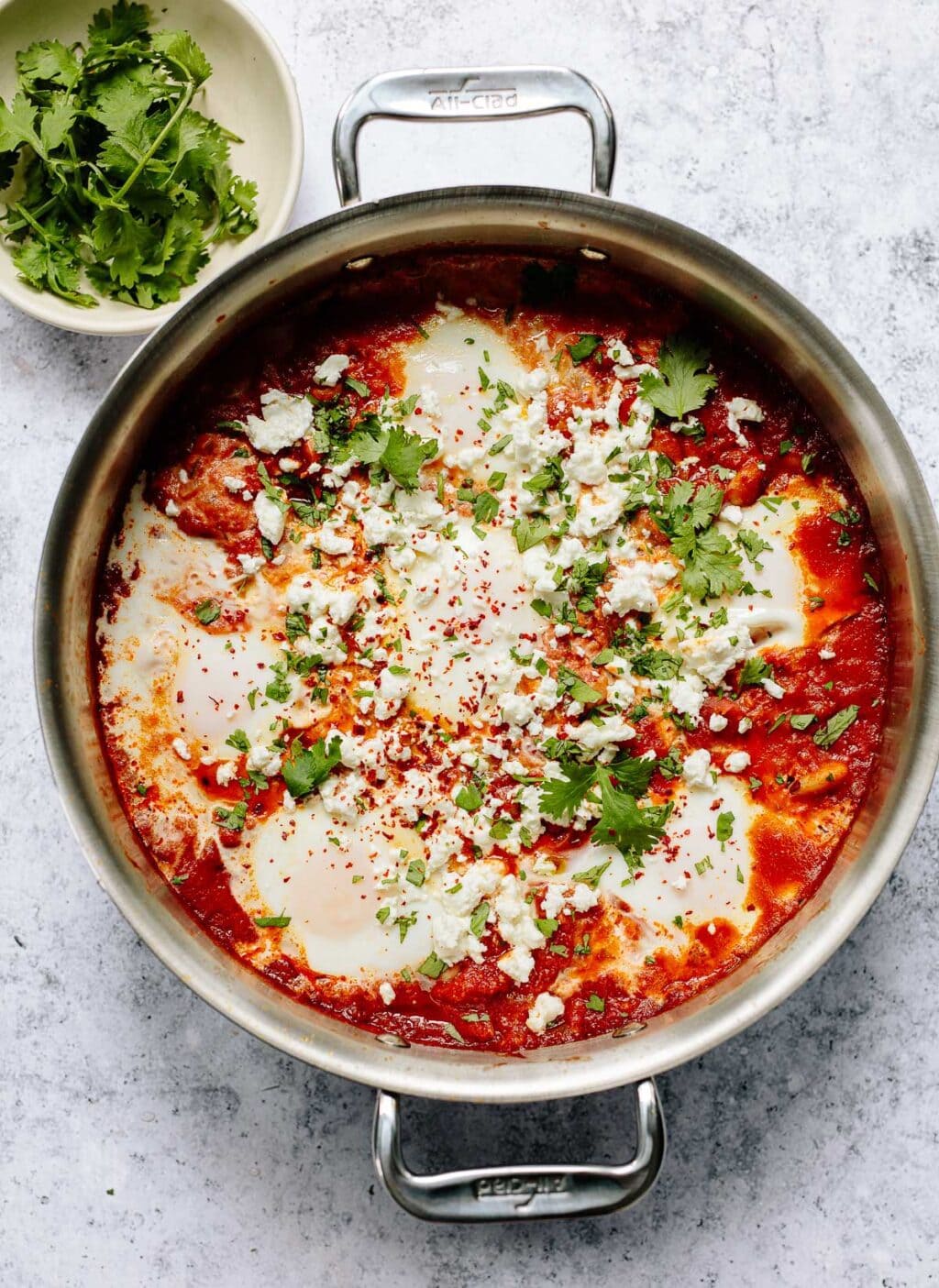 Soft poached eggs in a skillet with spiced tomato harissa sauce,topped with feta cheese and cilantro