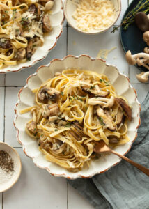 Bowl of fettuccine pasta topped with mushroom sauce, with cheese and forks
