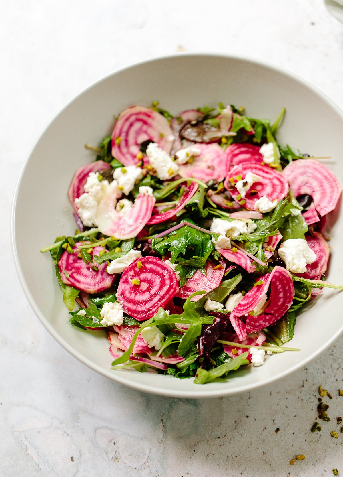 An image of striped Chioggia beets in a bowl tossed with greens and crumbled goat cheese.