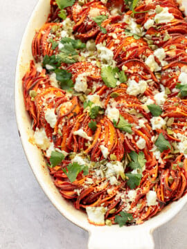 A sweet potato gratin with in an oval baking dish and a topping of goat cheese and pumpkin seeds.