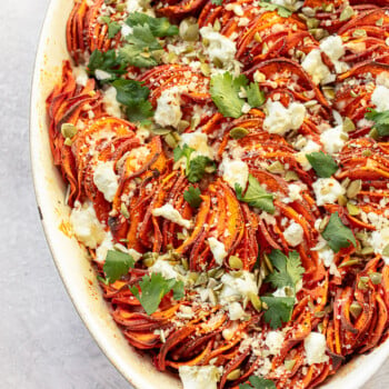 A sweet potato gratin with in an oval baking dish and a topping of goat cheese and pumpkin seeds.