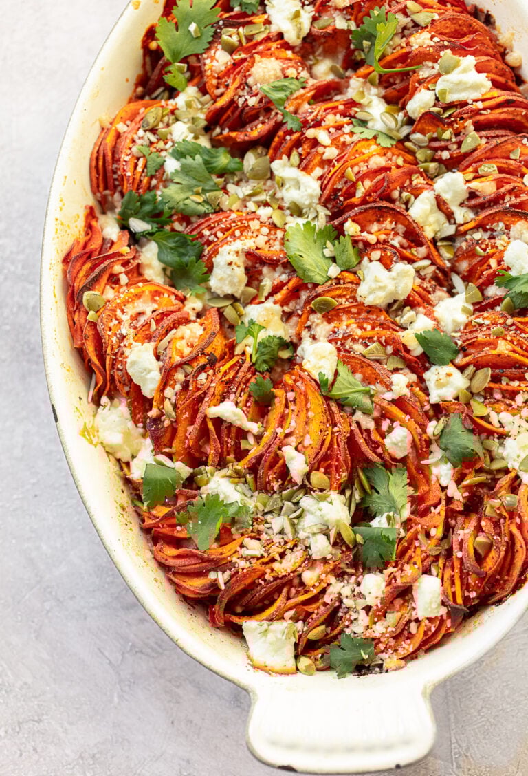 A sweet potato gratin with in an oval baking dish and a topping of goat cheese and pumpkin seeds.