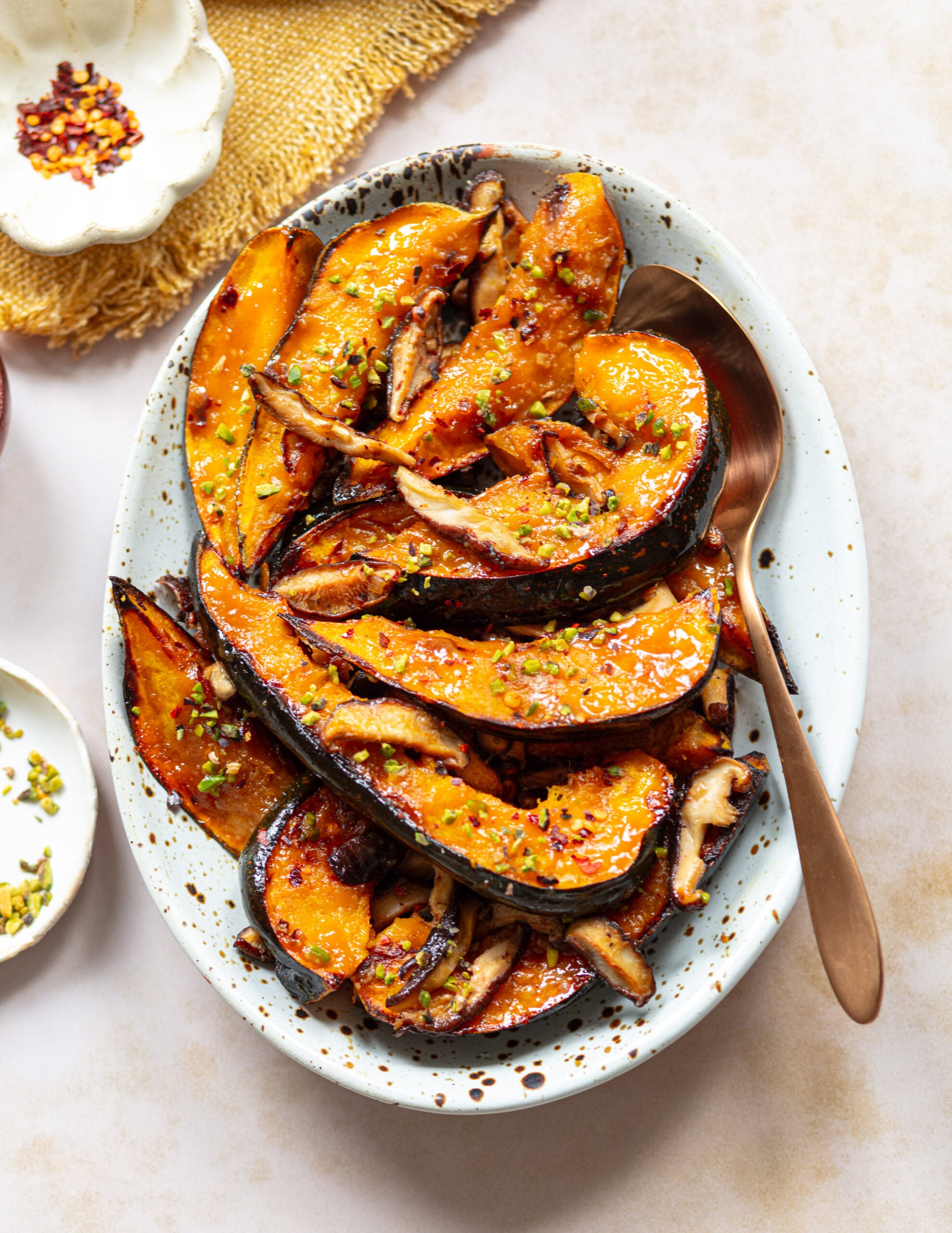 Miso-maple glazed acorn squash wedges on an oval platter, topped with seared shiitake mushrooms and chopped pistachios.
