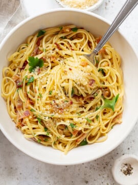 Pasta carbonara in a serving bowl, topped with grated cheese and chopped parsely.