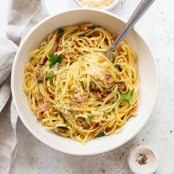 Pasta carbonara in a serving bowl, topped with grated cheese and chopped parsely.