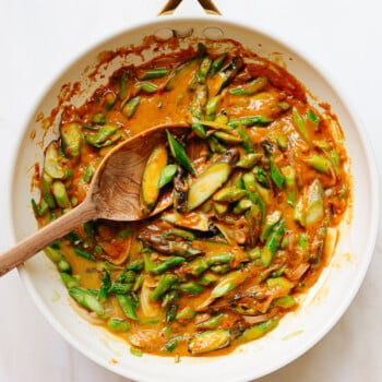 A skillet and wooden spoon stirring asparagus in peanut sauce.