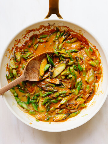 A skillet and wooden spoon stirring asparagus in peanut sauce.