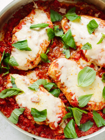 Chicken breasts with melted cheese and fresh basil leaves in a pan.