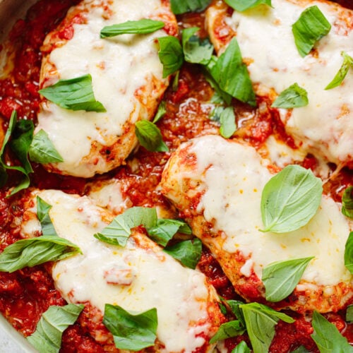Chicken breasts with melted cheese and fresh basil leaves in a pan.