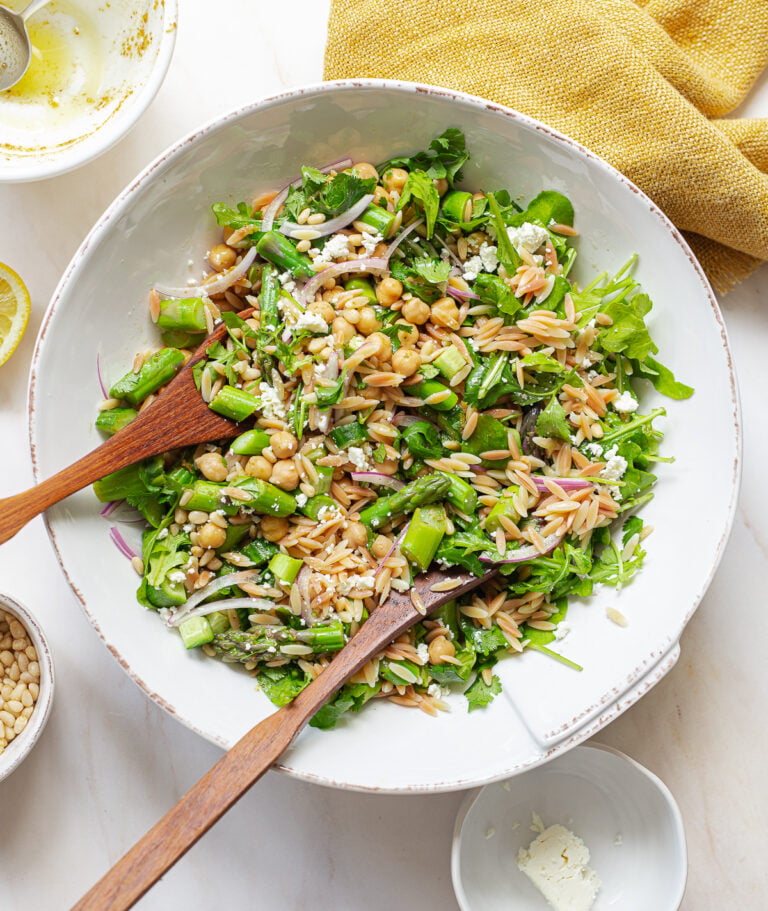A salad bowl full of orzo pasta salad and wooden servers.