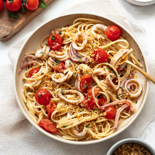 Spaghetti, roasted cherry tomatoes and squid in a bowl with a fork on the side.