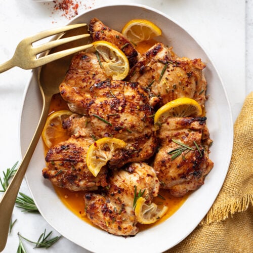 Cooked lemon chicken thighs on a platter with a serving spoon and fork.