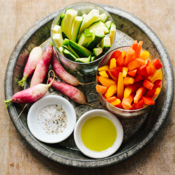 Raw vegetable sticks on a platter with olive oil, and a dish of salt and pepper.