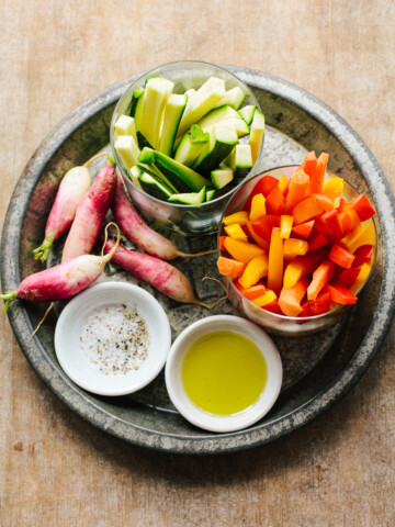 Raw vegetable sticks on a platter with olive oil, and a dish of salt and pepper.