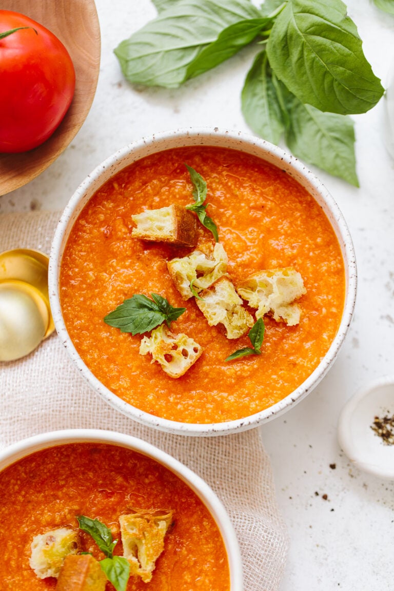 Tomato soup in a bowl, with croutons on top and fresh basil.