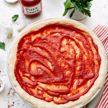 Pizza dough spread with pizza sauce on a work surface.