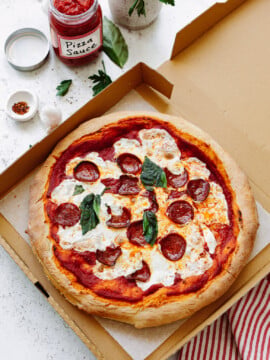A baked margarita pizza with pepperoni in a cardboard box.