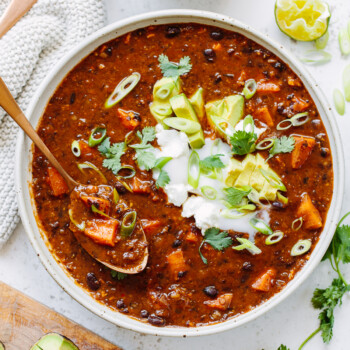 Black bean chili in a bowl with a spoon, with sliced avocado and chopped cilantro on top.
