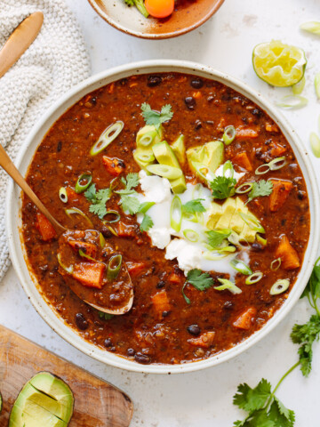 Black bean chili in a bowl with a spoon, with sliced avocado and chopped cilantro on top.