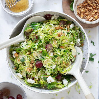 Shaved Brussels sprouts salad in a serving bowl, with serving spoons.