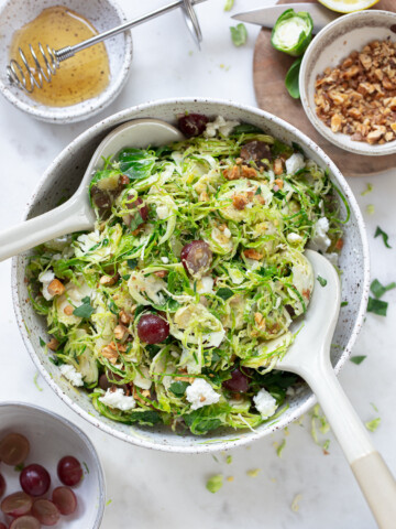 Shaved Brussels sprouts salad in a serving bowl, with serving spoons.
