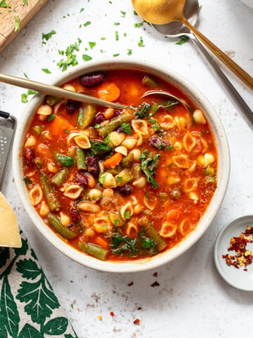 Vegetable soup with pasta shells in a serving bowl, with a spoon and grated cheese on the side.
