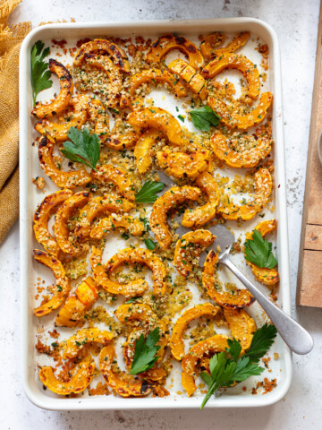 Sliced, roasted delicata squash on a baking sheet with a spatula.