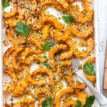 Sliced, roasted delicata squash on a baking sheet with a spatula.
