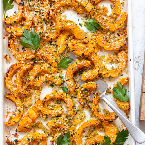 Sliced, roasted delicata squash on a baking sheet with a spatula.