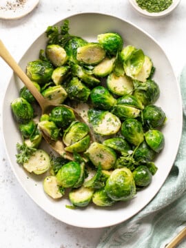 Buttered brussels sprouts on a platter with a serving spoon.
