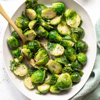 Buttered brussels sprouts on a platter with a serving spoon.