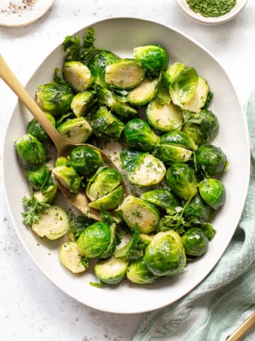 Buttered brussels sprouts on a platter with a serving spoon.