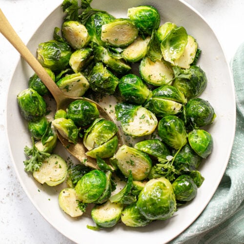 Buttered brussels sprouts on a platter with a serving spoon.