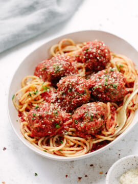 A white bowl filled with spaghetti topped with six large meatballs in marinara sauce, garnished with grated cheese and chopped herbs, with a fork resting on the side—a comforting classic perfect for your favorite dinner recipes.