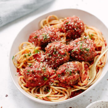 A white bowl filled with spaghetti topped with six large meatballs in marinara sauce, garnished with grated cheese and chopped herbs, with a fork resting on the side—a comforting classic perfect for your favorite dinner recipes.