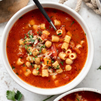 A bowl of chickpea and pasta soup with a spoon.