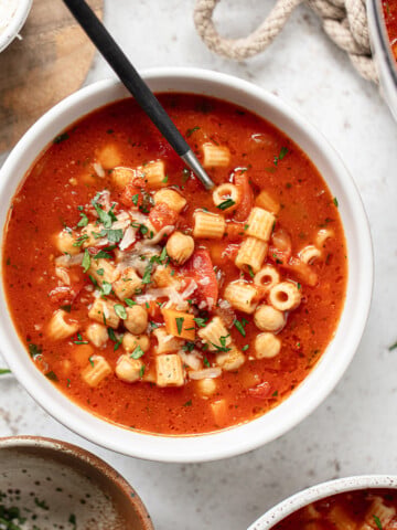 A bowl of chickpea and pasta soup with a spoon.