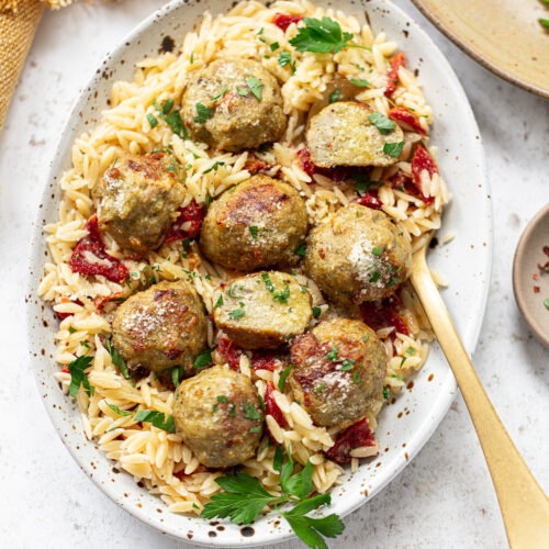 Chicken meatballs and orzo on a platter, with a spoon on the side.